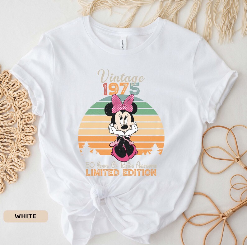 May include: White t-shirt with a vintage 1975 design featuring a cartoon image of Minnie Mouse in front of a sunset. The text "50 Years of Being Awesome Limited Edition" is printed below the image.