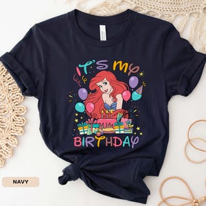 Puede incluir: Una camiseta azul marino con un gr&aacute;fico de Ariel de La Sirenita. El gr&aacute;fico muestra a Ariel con un pastel de cumplea&ntilde;os y el texto "It's My Birthday".