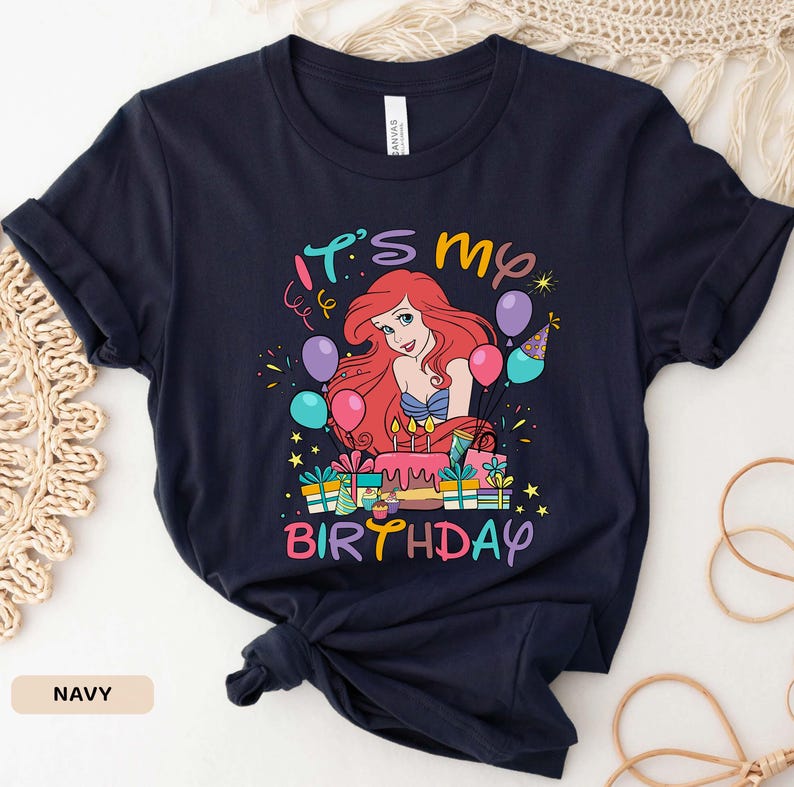 Puede incluir: Una camiseta azul marino con un gr&aacute;fico de Ariel de La Sirenita. El gr&aacute;fico muestra a Ariel con un pastel de cumplea&ntilde;os y el texto "It's My Birthday".