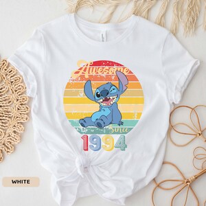 May include: White t-shirt with a vintage-style graphic of Stitch from Lilo & Stitch. The graphic says "Awesome Since 1994".