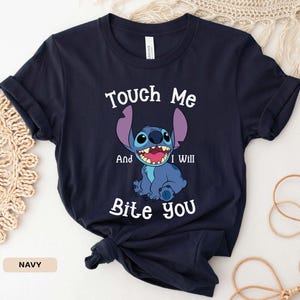 May include: A navy blue t-shirt with a cartoon Stitch character from Lilo & Stitch. The text "Touch Me And I Will Bite You" is printed on the shirt.