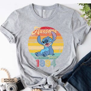 May include: Gray t-shirt with a vintage-style graphic of Stitch from Lilo & Stitch. The graphic features Stitch sitting with a wink and the text "Awesome Since 1994".