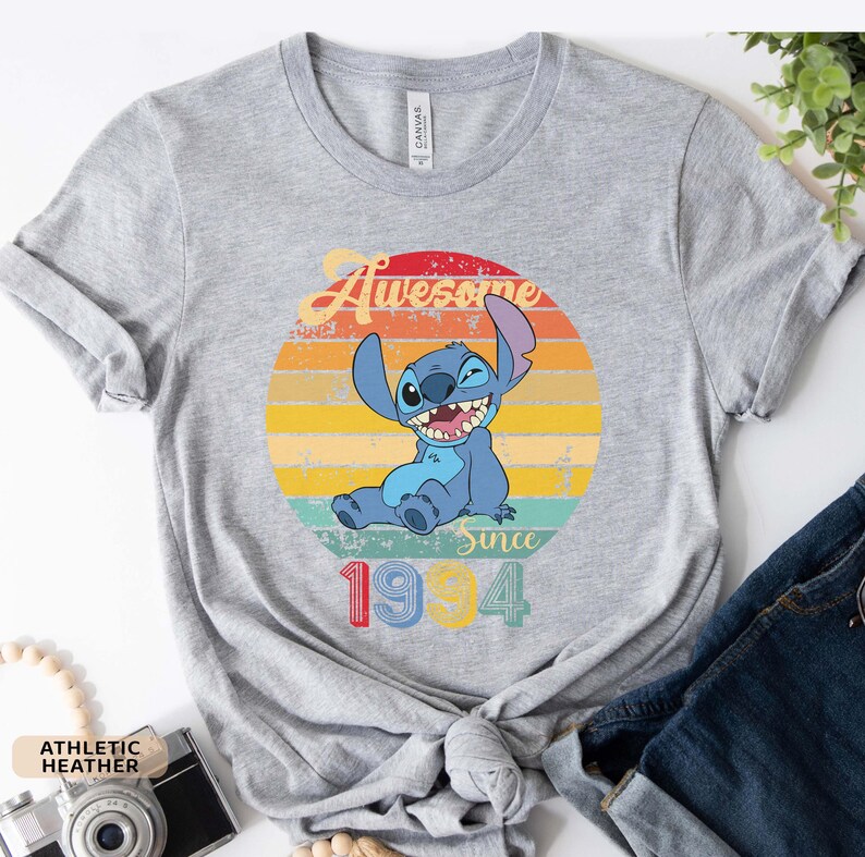 May include: Gray t-shirt with a vintage-style graphic of Stitch from Lilo & Stitch. The graphic features Stitch sitting with a wink and the text "Awesome Since 1994".