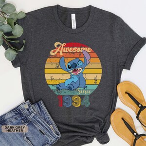 May include: Dark grey heather t-shirt with a vintage-style graphic of Stitch from Lilo & Stitch. The graphic says "Awesome Since 1994".