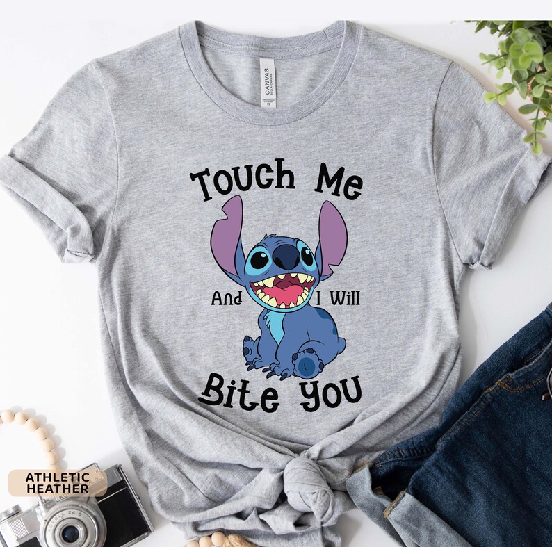 May include: A gray t-shirt with a blue cartoon character on it. The character is Stitch from Lilo & Stitch. The text on the shirt says "Touch Me And I Will Bite You".