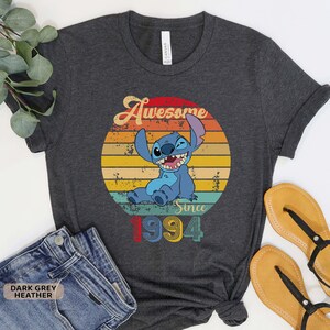May include: Dark grey heather t-shirt with a vintage-style graphic of Stitch from Lilo & Stitch. The graphic says "Awesome Since 1994".
