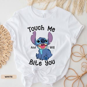 May include: White t-shirt with a blue Stitch character from Lilo & Stitch. The text "Touch Me And I Will Bite You" is printed on the shirt.