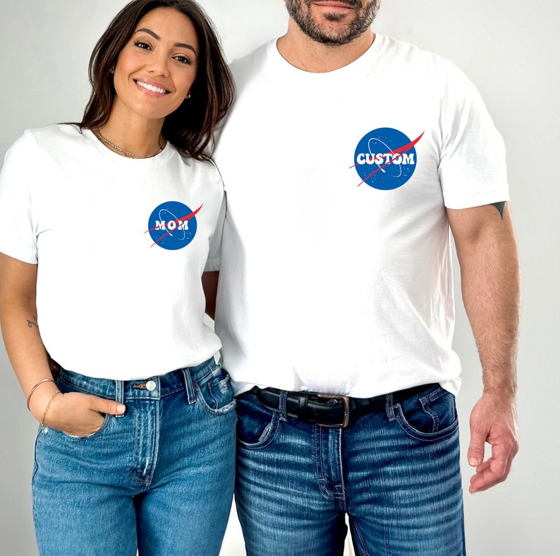 Op de afbeelding: Een stel draagt witte T-shirts met een blauw en rood NASA-ge&iuml;nspireerd logo. Het shirt van de vrouw zegt "MOM" en het shirt van de man zegt "CUSTOM".