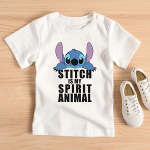 Op de afbeelding: Wit T-shirt met een blauw Stitch-personage uit Lilo & Stitch. De tekst "Stitch is my spirit animal" is in zwart onder het personage gedrukt.