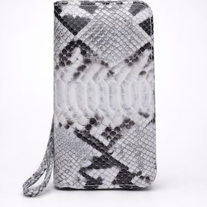 Peut inclure: Un portefeuille rectangulaire avec une dragonne, présentant un motif peau de serpent dans les tons de gris, noir et blanc. Le portefeuille a un design vertical avec un panneau central d'écailles plus claires.