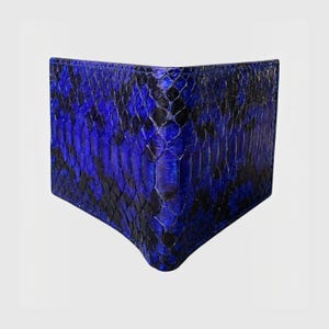 May include: A bifold wallet featuring a vibrant blue and black snakeskin pattern. The exterior displays a textured, scaled surface with a repeating diamond-like arrangement of dark and bright blue tones across the entire folded leather surface.