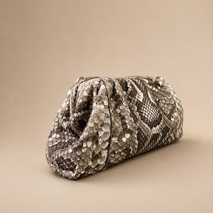 May include: A structured clutch bag featuring a textured snakeskin pattern in shades of gray, brown, and cream. The bag has a gathered, pouch-like silhouette with a soft, rounded shape and a concealed frame closure at the top.