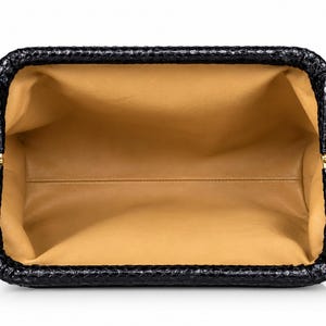 May include: An open rectangular clutch bag with a black exterior featuring a textured snakeskin pattern. The interior is lined with smooth tan leather. The frame of the bag is constructed with gold-toned metal hinges on both sides.