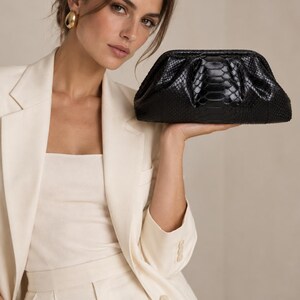 May include: A black clutch bag with a textured snakeskin pattern and a structured frame closure. The bag features a gathered, soft pouch shape with a glossy finish, providing a sleek and compact accessory for carrying essential items securely.