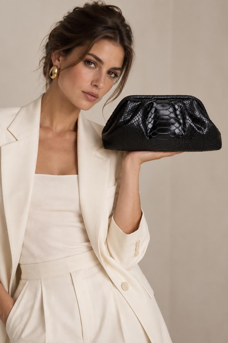 May include: A black clutch bag with a textured snakeskin pattern and a structured frame closure. The bag features a gathered, soft pouch shape with a glossy finish, providing a sleek and compact accessory for carrying essential items securely.