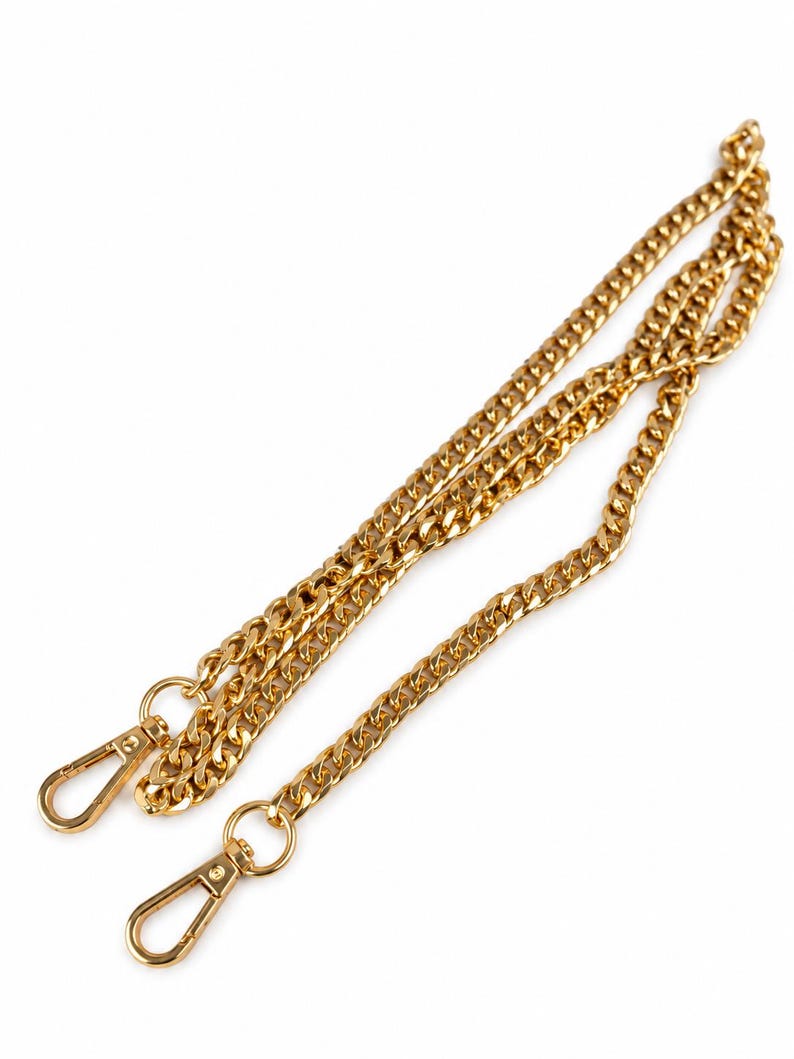 May include: A gold-toned metal chain strap featuring a curb link design. The chain is equipped with two matching gold-toned lobster claw clasps at each end, designed for attachment to bags or accessories, providing a secure and functional connection.