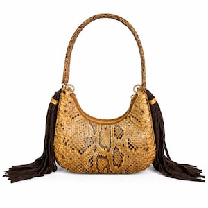 Könnte beinhalten: Eine halbmondförmige Schultertasche mit einem strukturierten goldbraunen Schlangenledermuster. Die Tasche verfügt über einen passenden Schlangenledergriff und lange, dunkelbraune Wildlederfransen, die mit goldfarbenen Beschlägen befestigt sind.