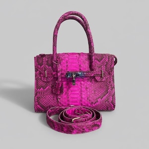 May include: A vibrant pink handbag with a snakeskin pattern, featuring a top handle and a detachable shoulder strap. The bag has a silver-tone clasp and hardware. The strap is approximately 40 inches long.