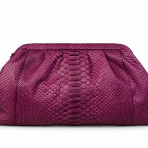 Pode incluir: Uma bolsa clutch magenta com um padr&atilde;o texturizado de pele de cobra. A bolsa tem uma estrutura arredondada com detalhes franzidos ao longo da borda superior, criando uma apar&ecirc;ncia suave e plissada na superf&iacute;cie frontal do acess&oacute;rio.