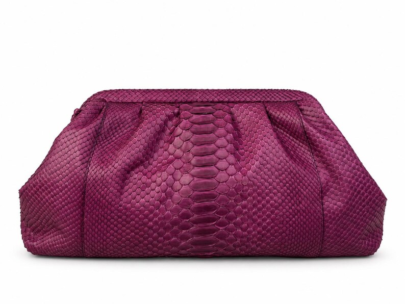 Pode incluir: Uma bolsa clutch magenta com um padr&atilde;o texturizado de pele de cobra. A bolsa tem uma estrutura arredondada com detalhes franzidos ao longo da borda superior, criando uma apar&ecirc;ncia suave e plissada na superf&iacute;cie frontal do acess&oacute;rio.