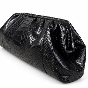 May include: A black clutch bag with a textured snakeskin pattern. The bag features a structured, elongated rectangular shape with a gathered top closure and a glossy finish that highlights the intricate scale details across the entire surface.