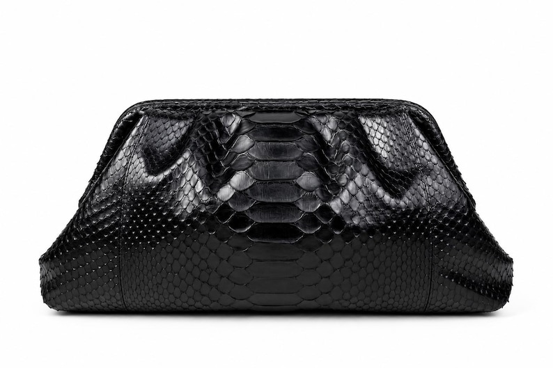 May include: A black clutch bag featuring a textured snakeskin pattern with a glossy finish. The bag has a structured frame with a hinged opening at the top, characterized by a wide, tapered shape and a smooth, dark surface texture throughout.