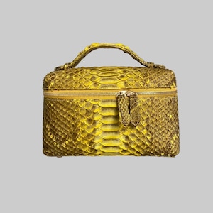 Puede incluir: Un neceser amarillo rectangular con asa y cierre de cremallera. La bolsa está hecha de un material similar a la piel de serpiente, con un patrón texturizado en forma de escamas. La cremallera y el asa son del mismo color amarillo.