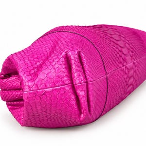 May include: A bright fuchsia clutch bag featuring a textured snakeskin pattern. The bag has a folded, structured design with visible seams and a smooth, consistent color throughout the exterior surface, showcasing a detailed scale-like texture.