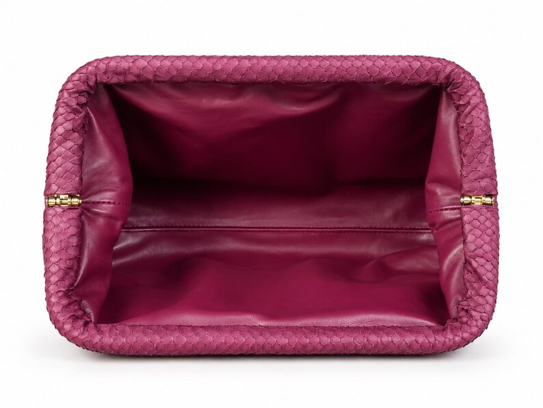 Pode incluir: Uma bolsa clutch magenta com um padr&atilde;o exterior texturizado semelhante a escamas e um forro interior liso de cor magenta s&oacute;lida. A bolsa retangular possui uma abertura de moldura articulada com pequenas dobradi&ccedil;as met&aacute;licas douradas.