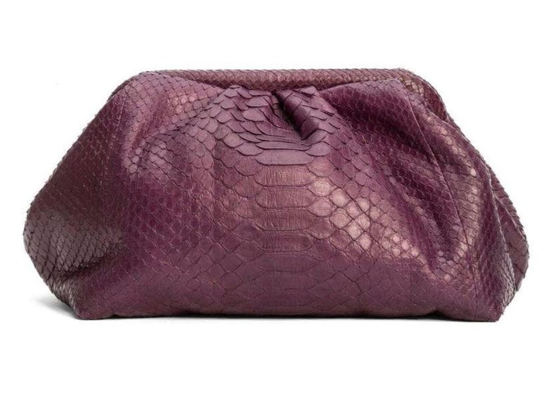 May include: A deep purple clutch bag featuring a textured snakeskin pattern. The bag has a soft, gathered, pouch-like silhouette with a hinged frame closure at the top, creating a rounded shape that tapers toward the bottom edges.