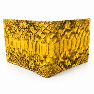 May include: A gold-colored wallet with a snakeskin pattern. The wallet is rectangular and appears to be made of leather. The scales are visible and create a textured surface. The wallet is empty and sits on a white background.