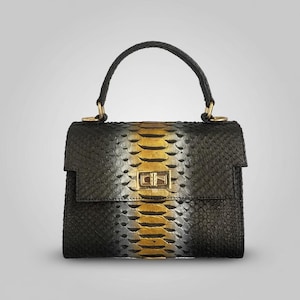Könnte beinhalten: Schwarze Handtasche mit Schlangenmuster und einem gold-gelben Streifen in der Mitte. Die Tasche hat einen oberen Griff und einen goldenen Verschluss. Die Tasche ist etwa 20 cm breit und 15 cm hoch.