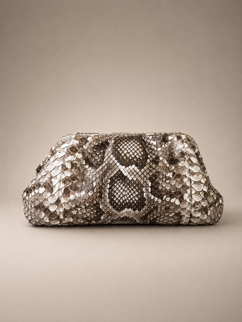 May include: A structured clutch bag featuring a textured snakeskin pattern in shades of brown, gray, and cream. The bag has a rounded, soft-sided rectangular shape with a frame closure, showcasing a detailed scale design across the entire exterior.