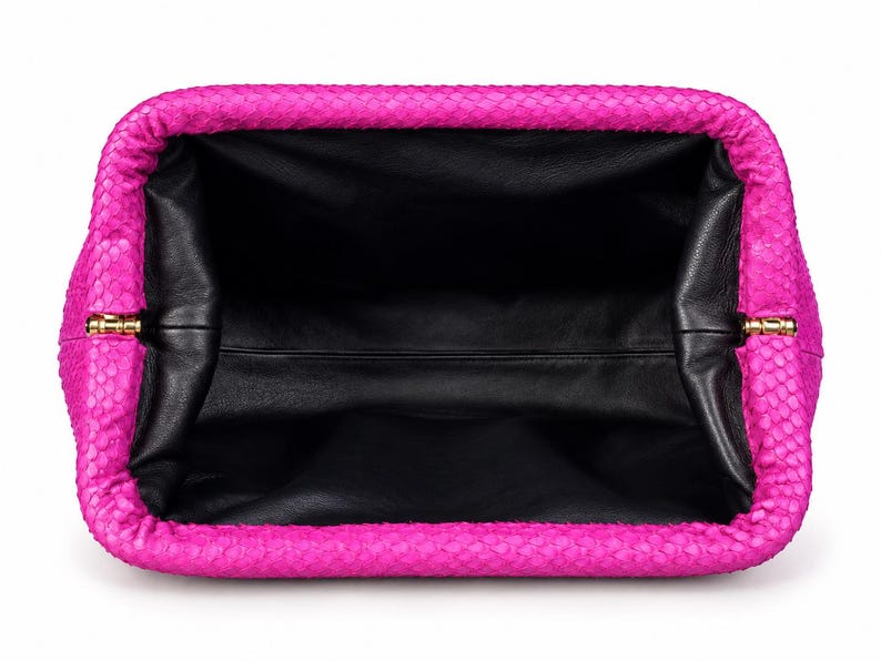 May include: A bright fuchsia clutch bag with a textured snakeskin-patterned exterior and a wide, open rectangular frame. The interior is lined with smooth black leather, and the frame features small gold-toned metal hinges on both sides.