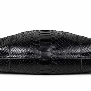 May include: A black handbag featuring a textured snakeskin pattern across its entire surface. The bag has a rounded, elongated shape with visible seams along the sides and a glossy finish that reflects light across the scales.