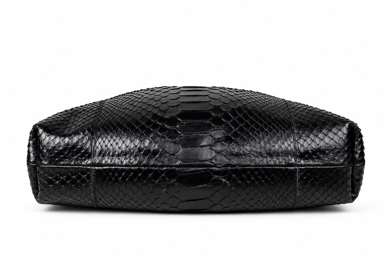 May include: A black handbag featuring a textured snakeskin pattern across its entire surface. The bag has a rounded, elongated shape with visible seams along the sides and a glossy finish that reflects light across the scales.