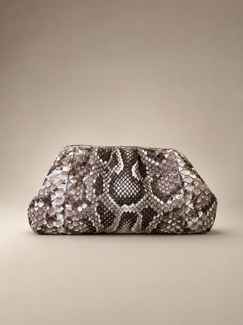 May include: A structured clutch bag featuring a detailed snakeskin pattern in shades of brown, gray, and white. The bag has a rounded, gathered top frame design with a textured, scale-like surface throughout the exterior, creating a distinct visual pattern.