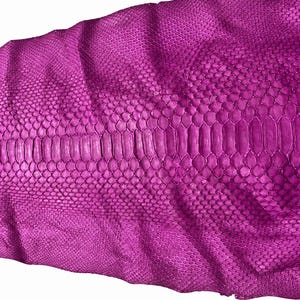 May include: A vibrant magenta snakeskin leather hide featuring a distinct central row of large, elongated scales flanked by smaller, uniform hexagonal scales on both sides, showcasing a natural, textured pattern throughout the entire surface.