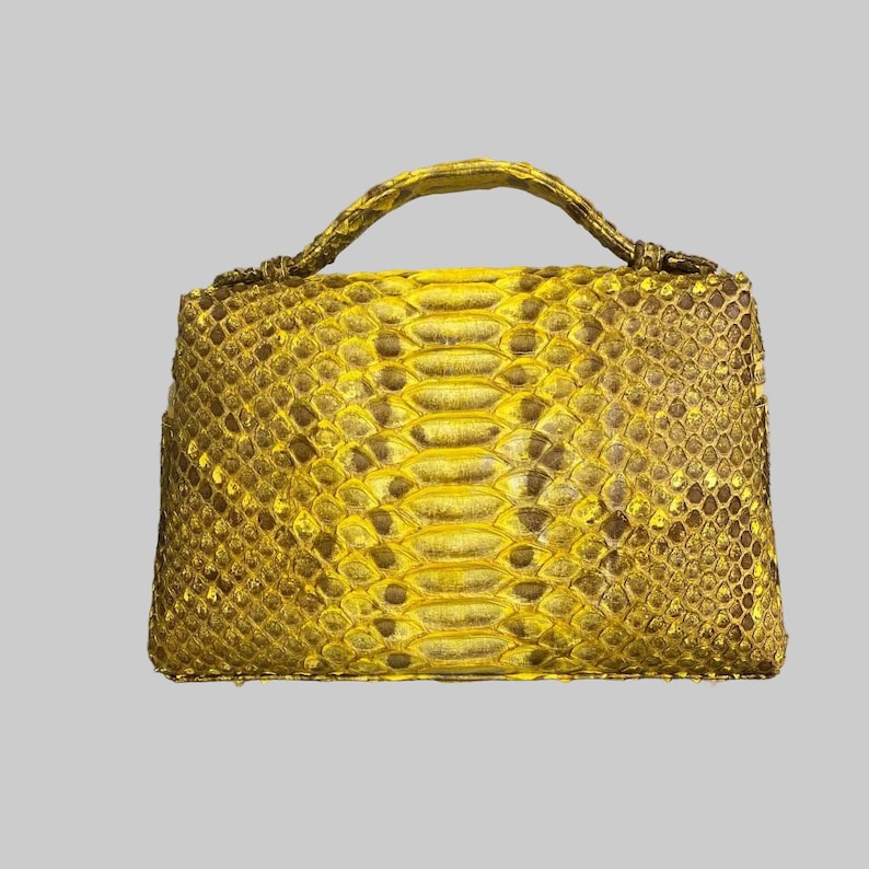 May include: A structured handbag featuring a vibrant yellow and metallic gold snakeskin pattern. The bag has a rectangular body with a single arched top handle, showcasing a detailed, repeating scale texture across the entire exterior surface.