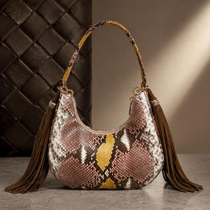Könnte beinhalten: Eine halbmondförmige Handtasche mit Schlangenledermuster in den Farben Rosa, Weiß, Braun und Gelb. Die Tasche verfügt über einen einzelnen Tragegriff und lange braune Wildlederfransen, die seitlich mit goldfarbenen Metallbeschlägen befestigt sind.