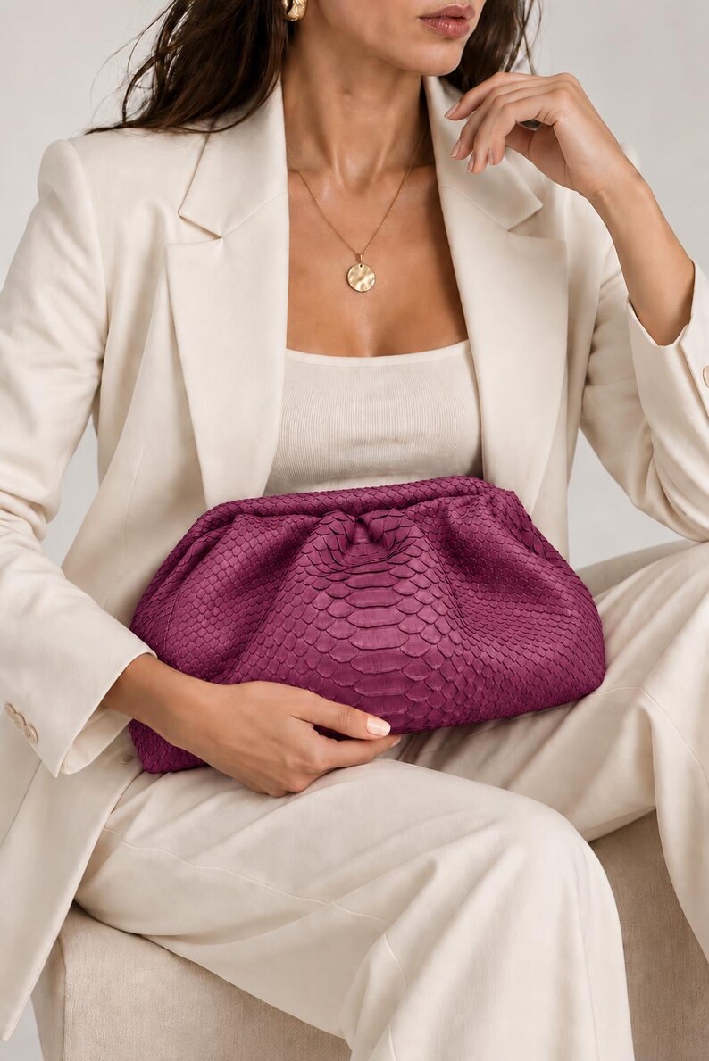 Pode incluir: Uma bolsa clutch magenta profunda com um padr&atilde;o de pele de cobra texturizado e um design franzido de estrutura macia. O acess&oacute;rio tipo bolsa tem uma silhueta arredondada e um fecho de dobradi&ccedil;a, exibindo uma cor rica, saturada e textura.