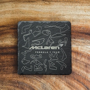 May include: Black slate coaster featuring a white outline of various racetracks and the text "McLaren Formula 1 Team".