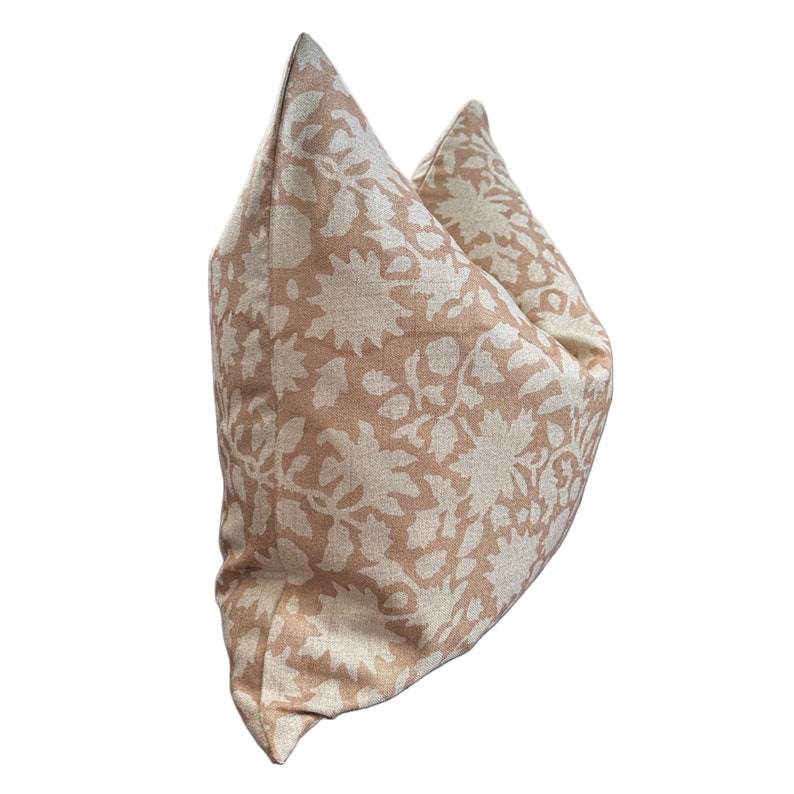 May include: A beige pillow with a white floral pattern. The pillow is made of a soft, textured fabric.