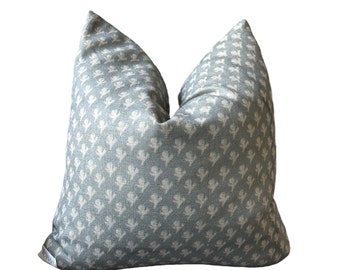 Könnte beinhalten: Ein quadratisches Zierkissen mit einem hellgrauen Stoffbezug und einem sich wiederholenden Muster aus kleinen, cremeweißen Blumenmotiven. Das Kissen hat eine weiche, leicht eingedrückte Oberkante und ein kleines weißes Stoffetikett mit Text.