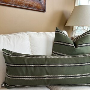 May include: Two decorative throw pillows with a green and white striped pattern. The pillows are on a white couch.