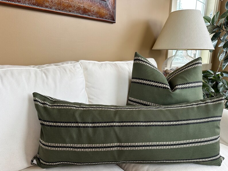 May include: Two decorative throw pillows with a green and white striped pattern. The pillows are on a white couch.