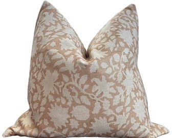 May include: A square throw cushion featuring a light beige and soft tan floral pattern. The fabric displays a dense, repeating botanical design with stylised leaves and blossoms covering the entire surface of the cushion, which is plumped at the top.
