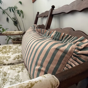 Könnte beinhalten: Eine Holzbank mit einem gestreiften Kissen und einem Kissen mit Blumenmuster. Die Bank ist aus dunklem Holz und hat ein schlichtes Design.