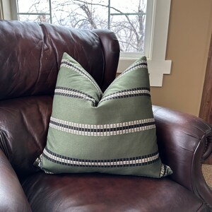 May include: A green and black striped throw pillow on a brown leather armchair.