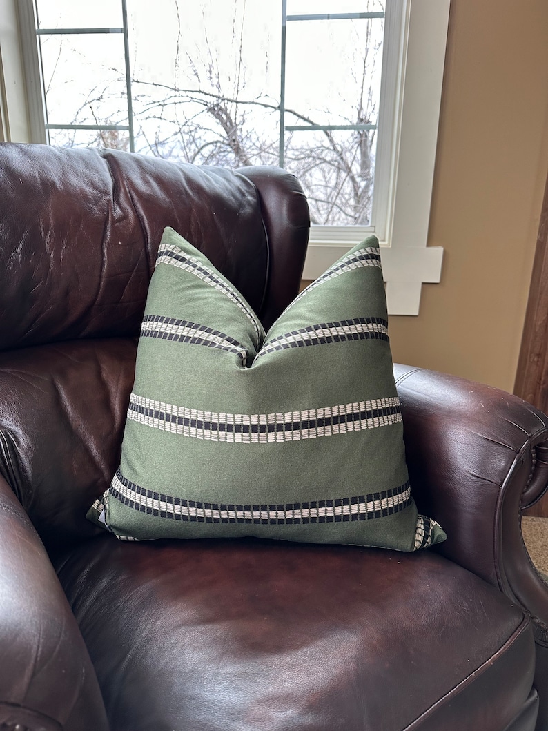 May include: A green and black striped throw pillow on a brown leather armchair.